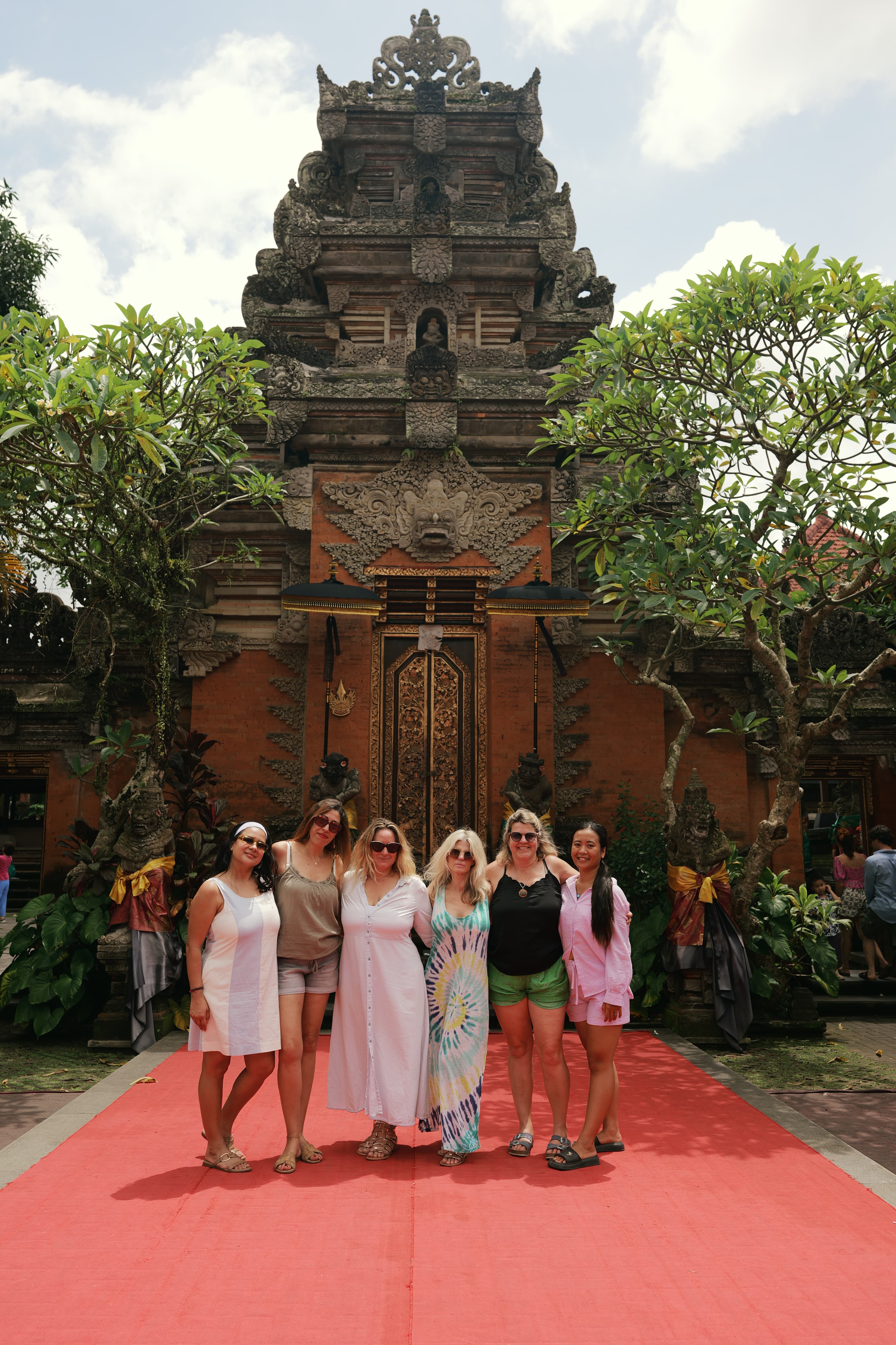 Six femmes posent sur un tapis rouge devant l'entrée ornée d'un temple balinais traditionnel.