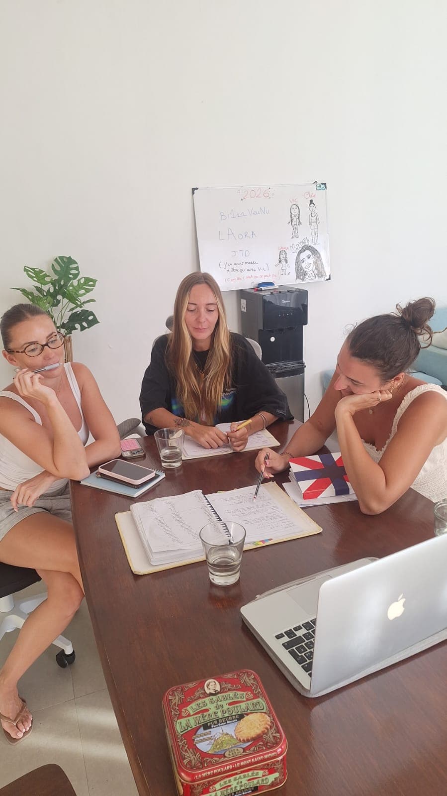 Trois femmes travaillent ensemble autour d'une table avec des cahiers et un ordinateur.