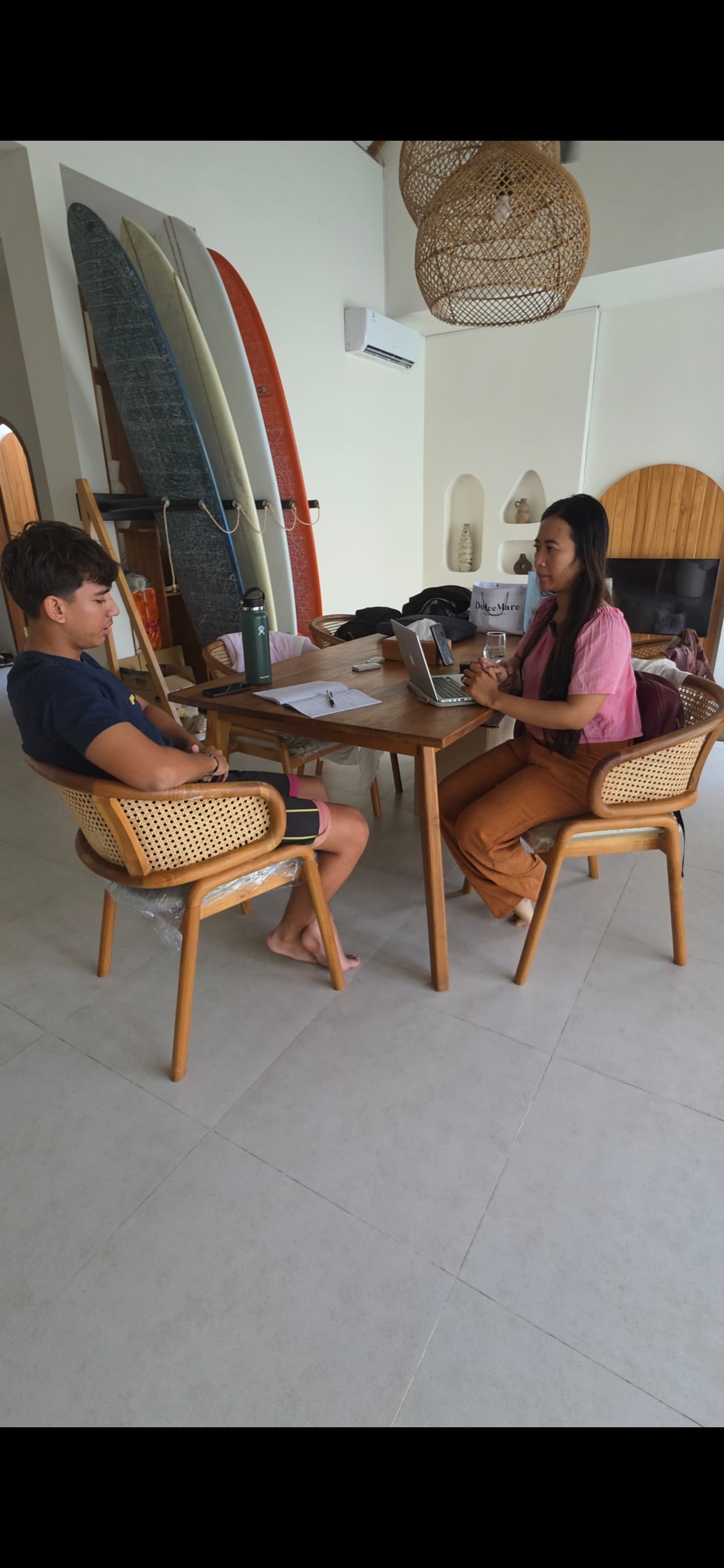Homme et femme travaillant à une table en bois avec ordinateur et planches de surf.