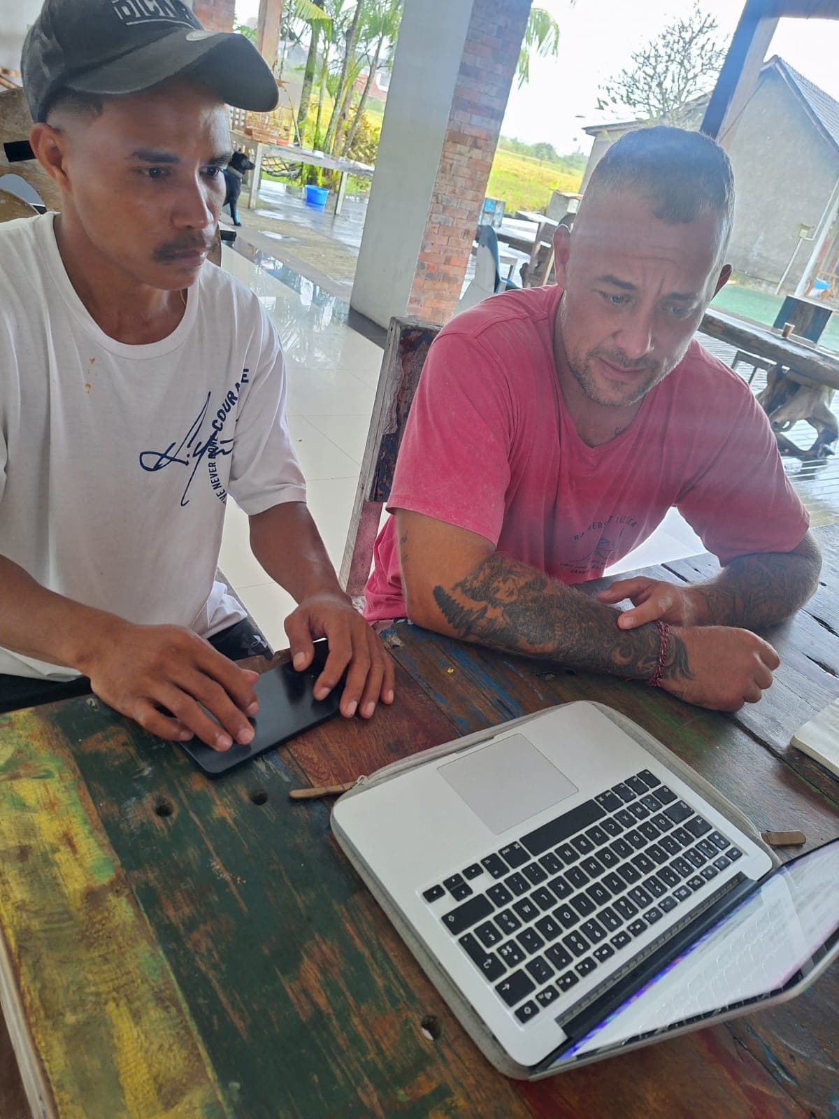 Deux hommes collaborent sur un ordinateur portable posé sur une table en bois rustique.